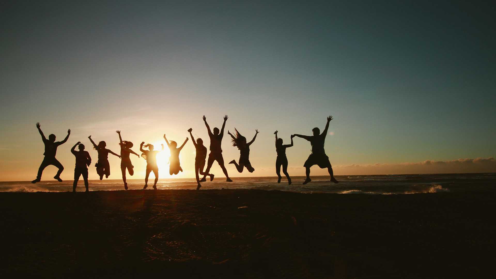 people are jumping on the beach during sunset